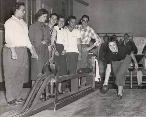 Black and white photograph of young adults playing bowling. They have fun.