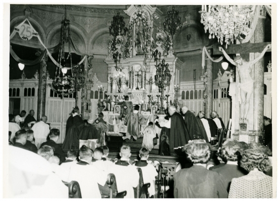 Black and white photograph of clerics praying at the altar of a church. Other clerics and lay people attend the ceremony.