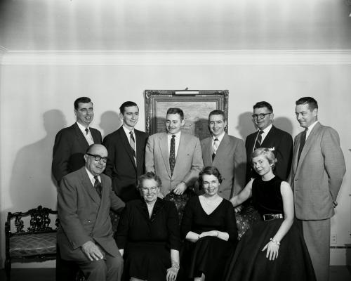 Black and white family photograph. Standing in the back, two middle-aged men and four young men. Sitting in front, an older man and woman, and two young women. The men all wear suits; the women wear black dresses.