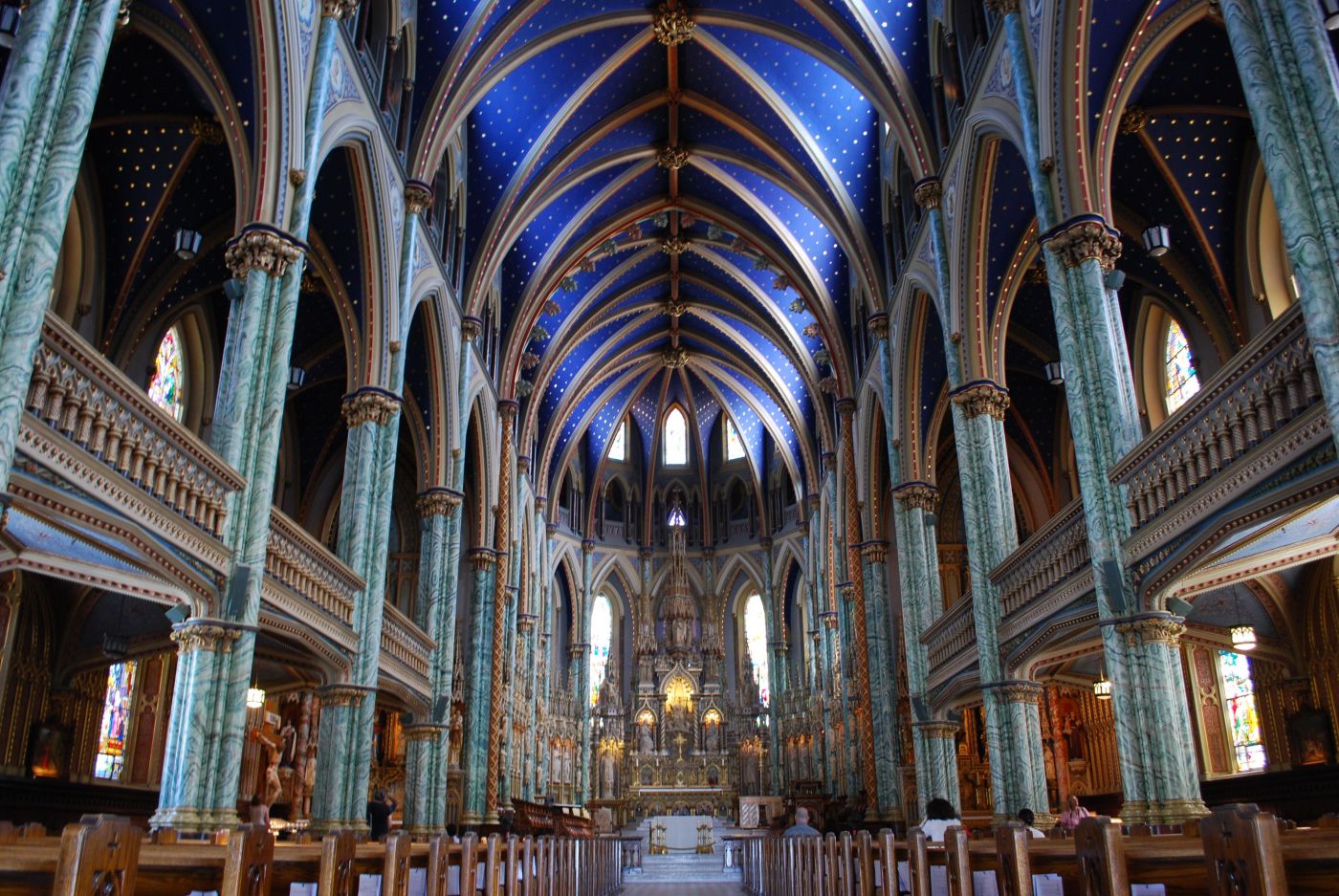 Colour photograph of the interior of a neo-Gothic-style church. Columns of green and white marble line the nave on each side. The vaulted ceiling is painted blue. The sanctuary is richly carved.