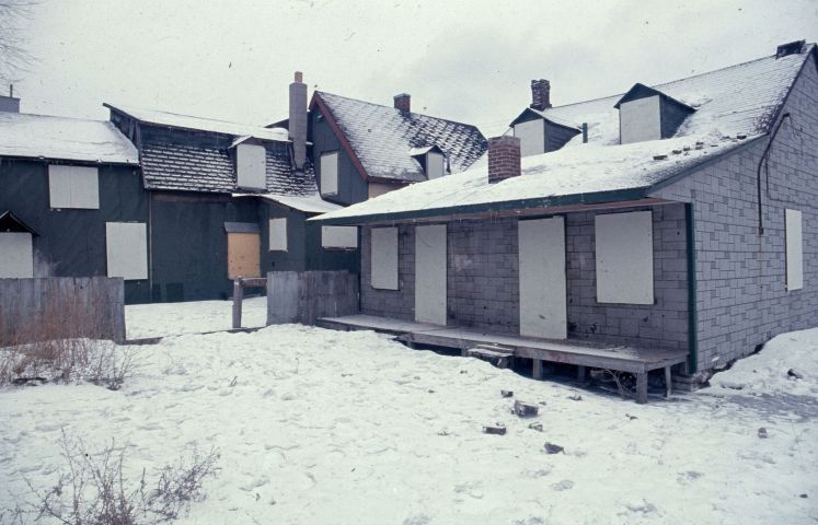 Colour photograph of four houses boarded-up in a winter landscape.